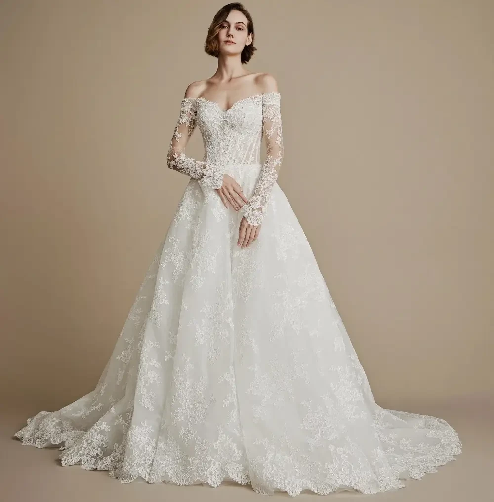 A model wearing a beautiful off-shoulder wedding dress with long lace sleeves and a flowing skirt against a neutral background.