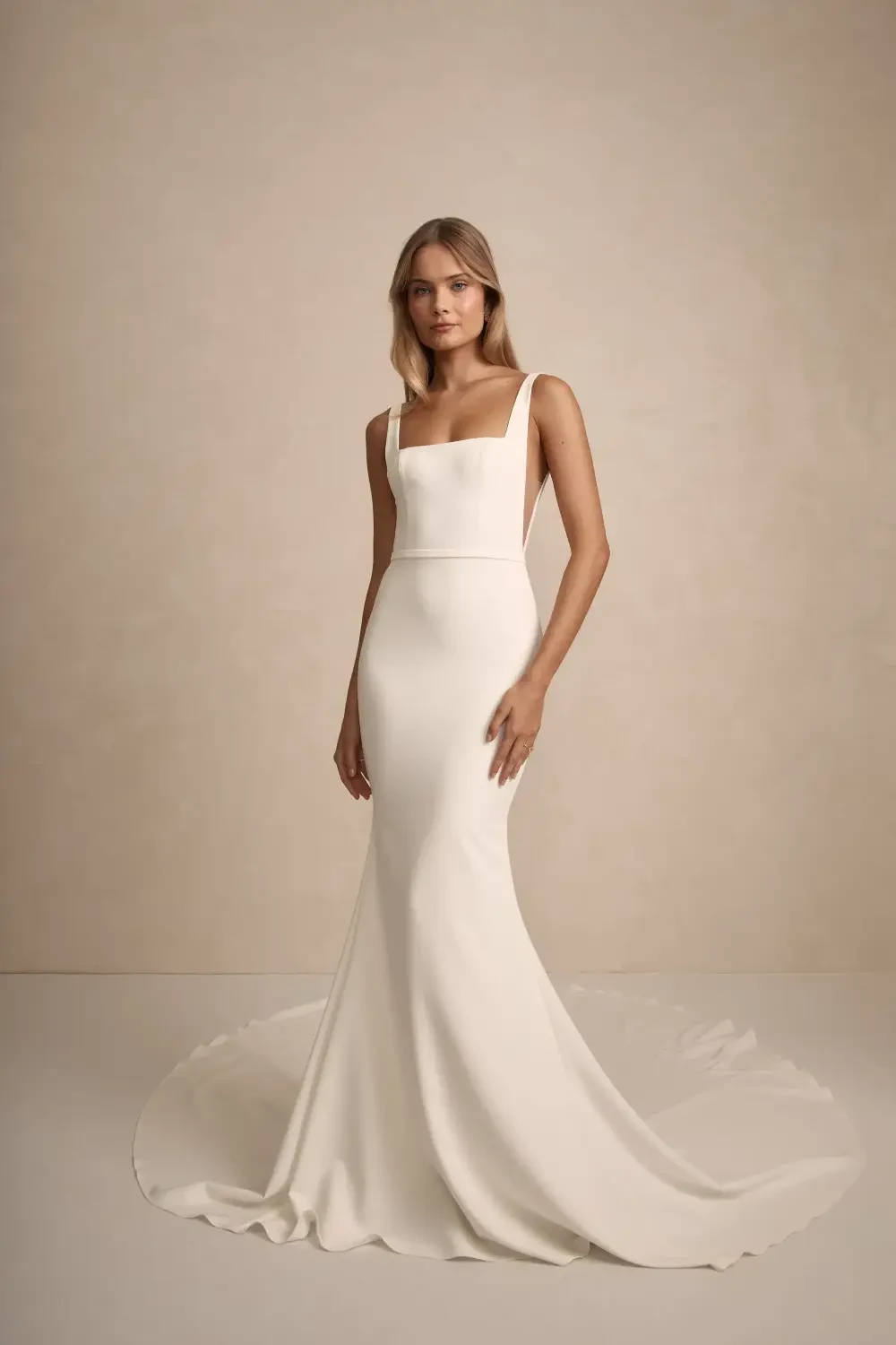 A woman wearing a form-fitting white dress with a square neckline, standing elegantly against a neutral background.